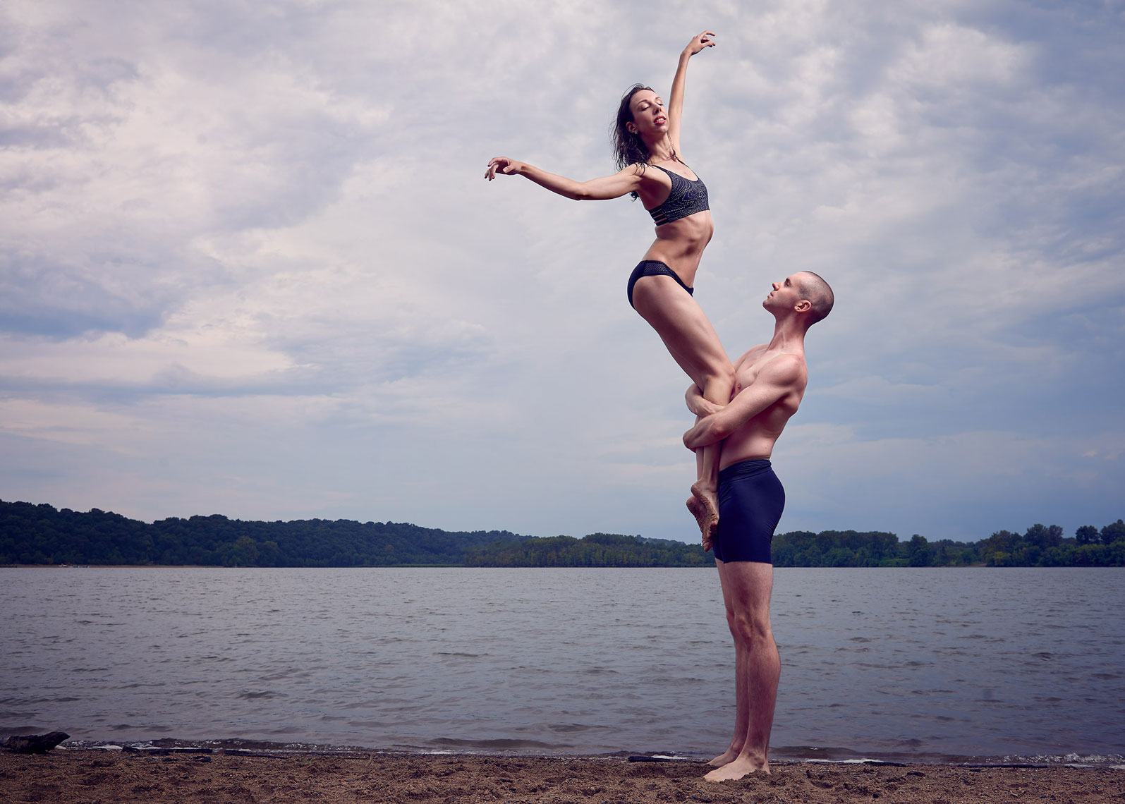 Ballet couple standing tall next to lake.
