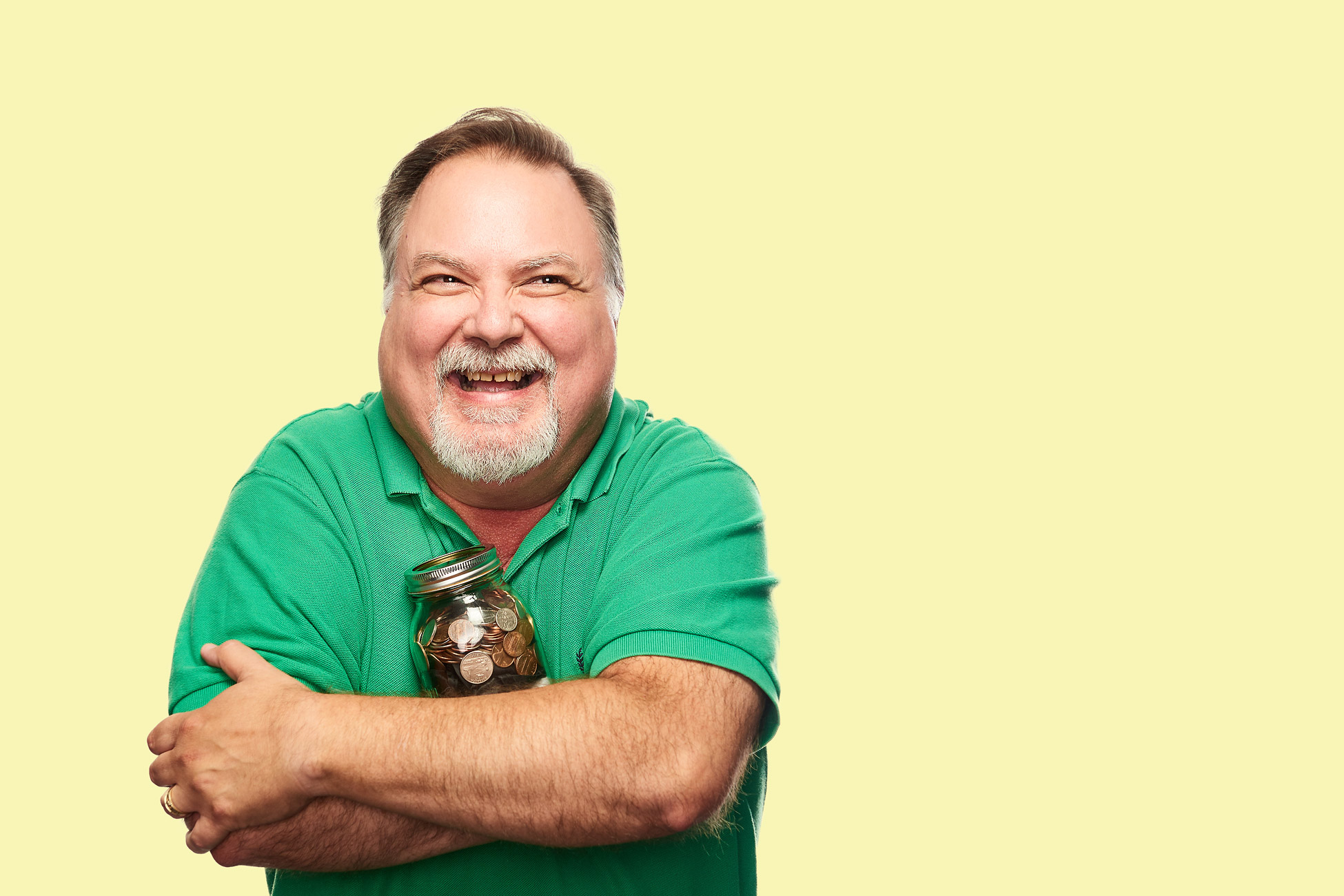 Man in green shirt  holding piggy bank on yellow background.