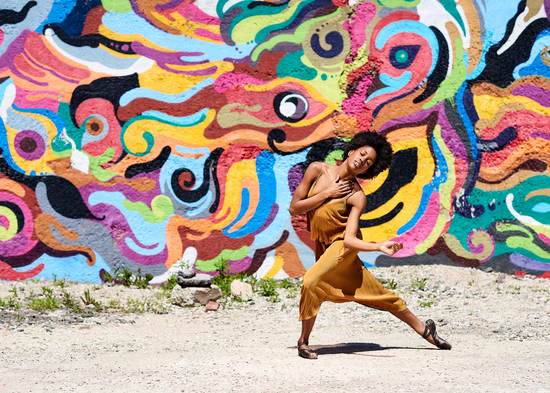 African American ballet dancer posing with colorful wall behind her.